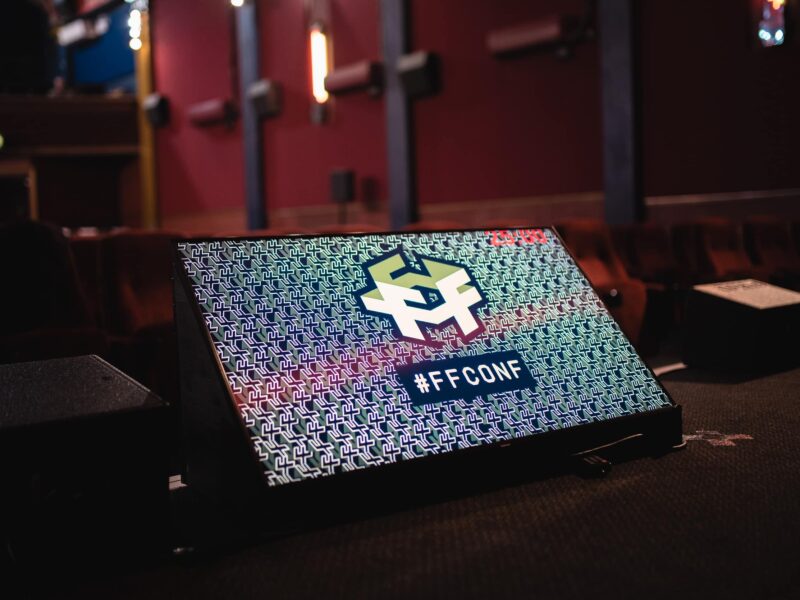 A screen on a stage with the ffconf logo and hashtag