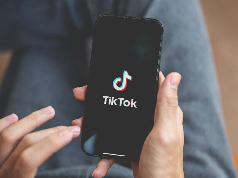 Person sitting down with legs crossed holding a phone rested on their legs with the TikTok logo on a dark screen