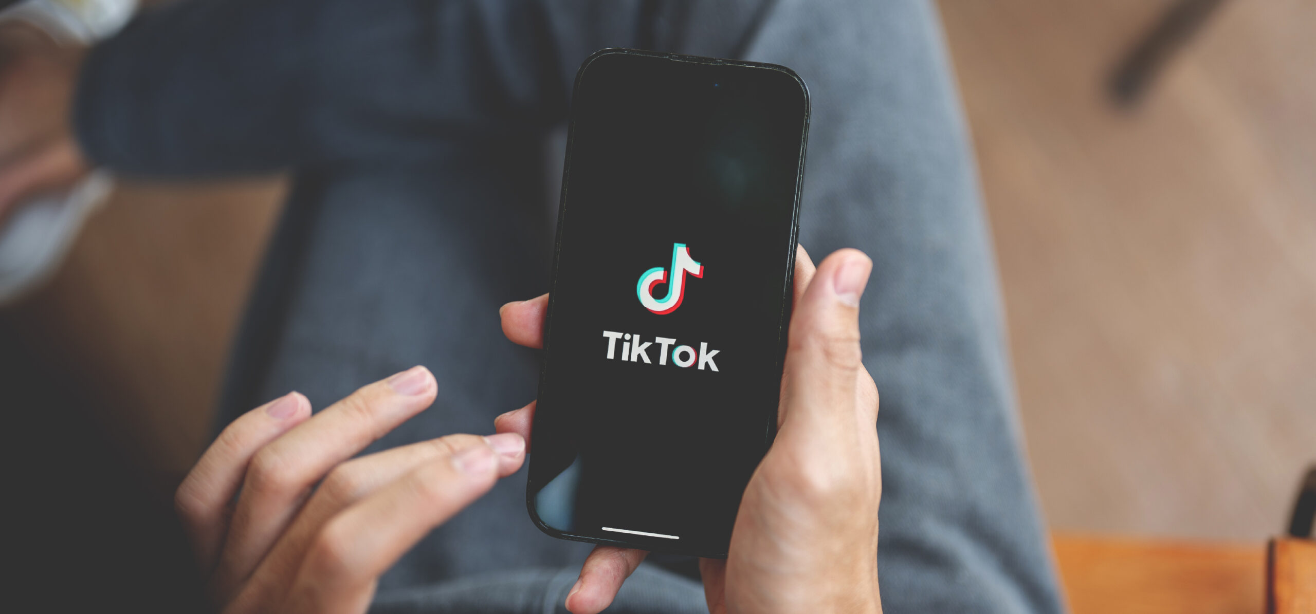Person sitting down with legs crossed holding a phone rested on their legs with the TikTok logo on a dark screen