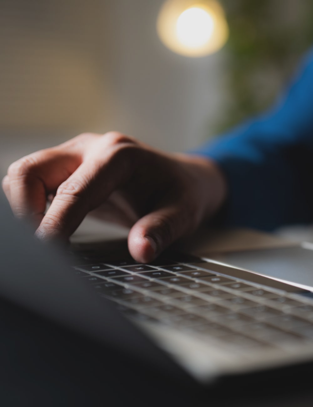 close up of a man wearing a blue long sleeve shirt typing on a laptop