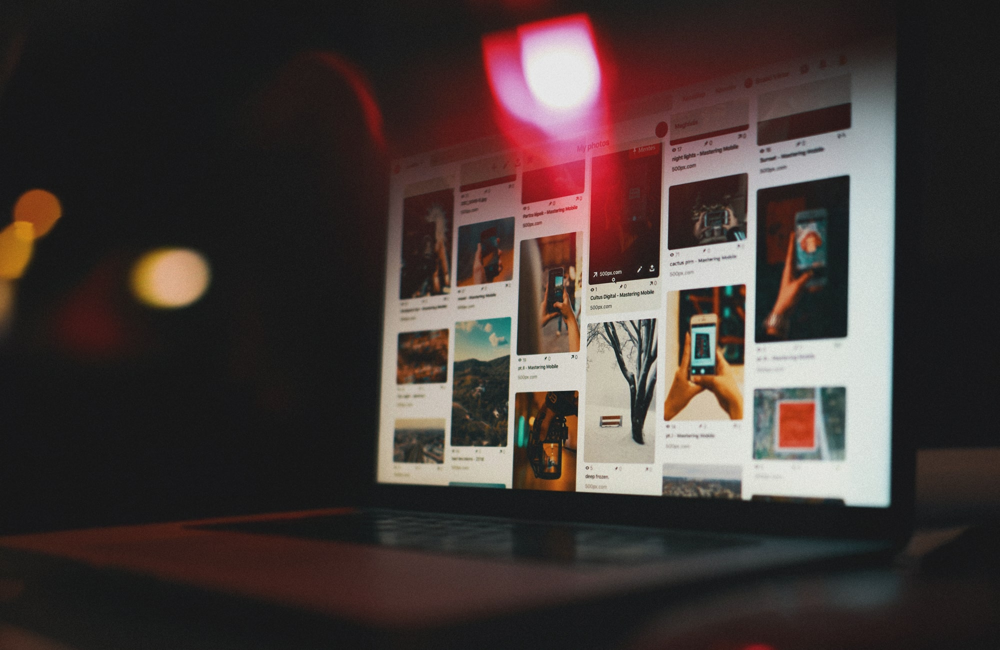 A laptop screen glowing in a dark room, displaying a Pinterest gallery of various photos and pins, with a soft red light reflecting across the top of the screen.