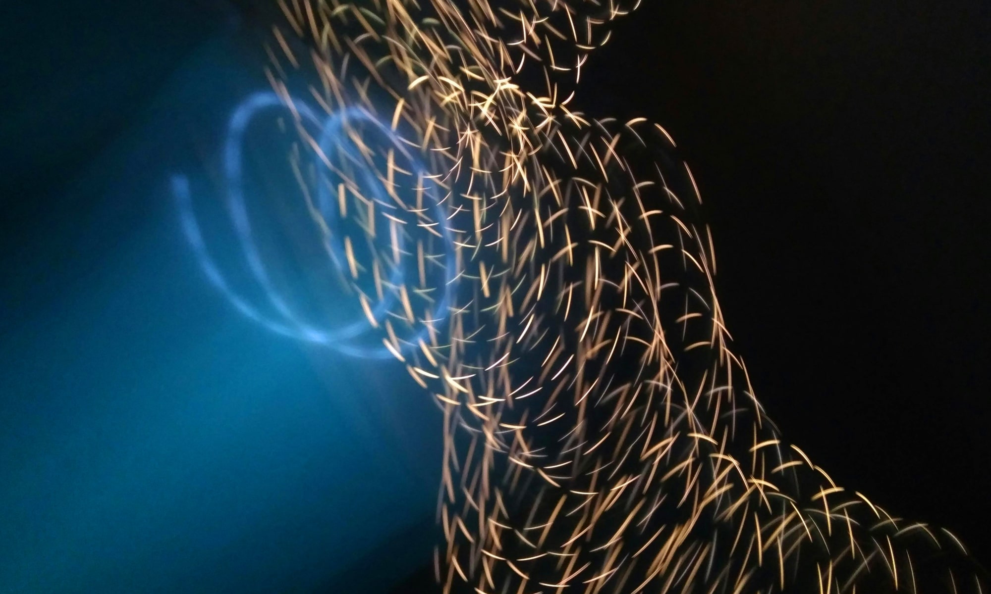 Abstract light trails forming a flowing, wave-like pattern of golden sparks and soft blue glow against a dark background.