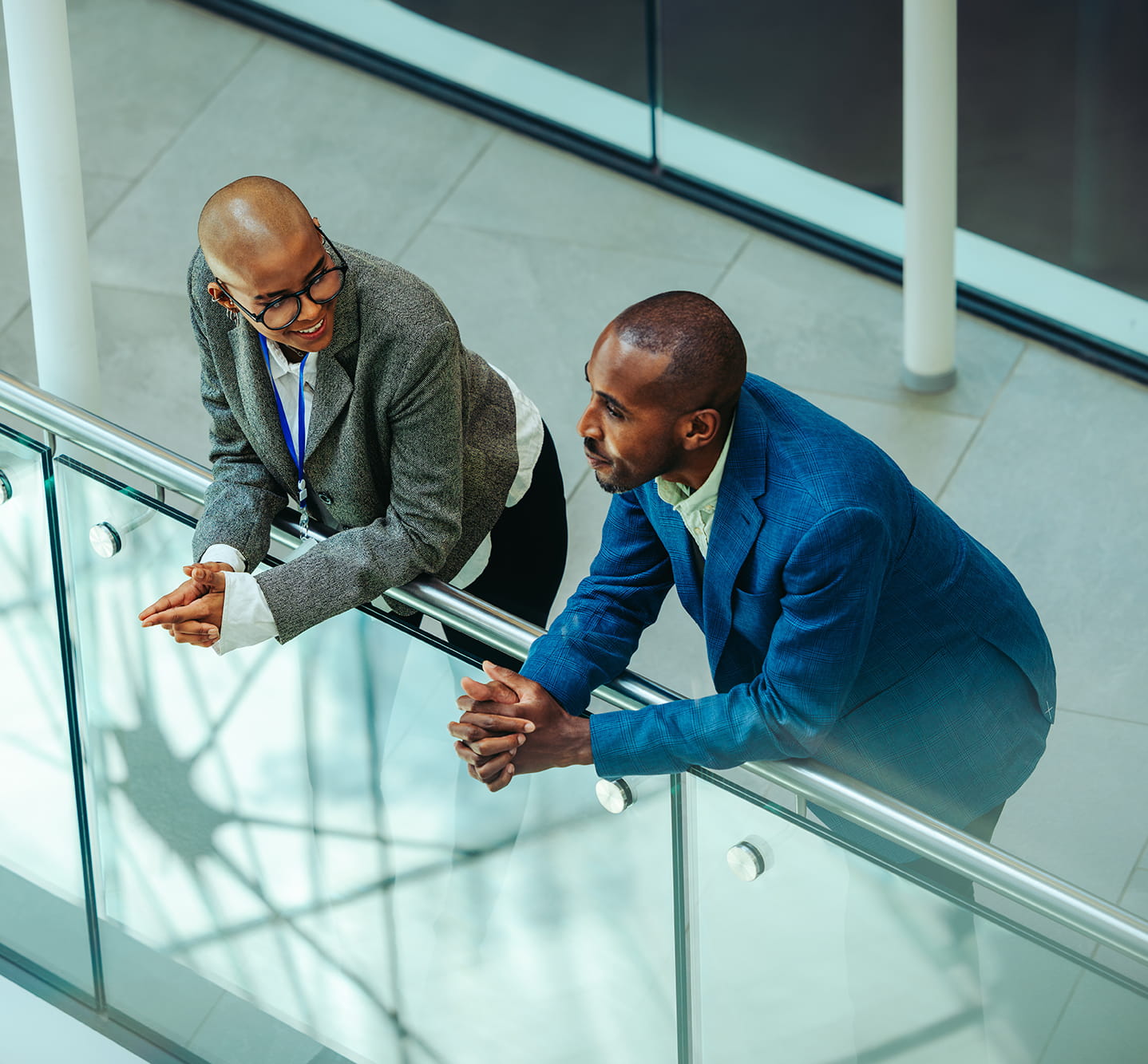Two professionals talking while leaning on an office balcony.
